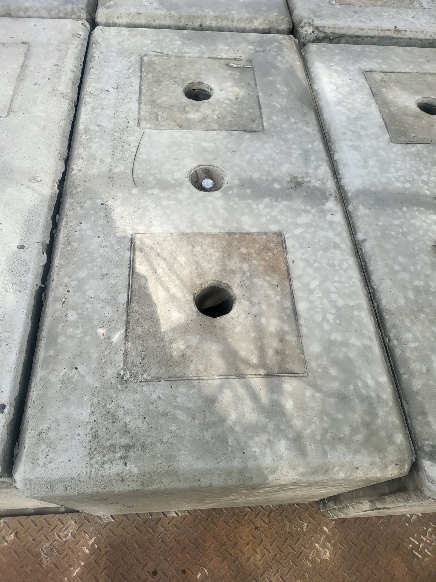 Close-up of concrete slabs with circular holes in the center placed on a textured metal surface.